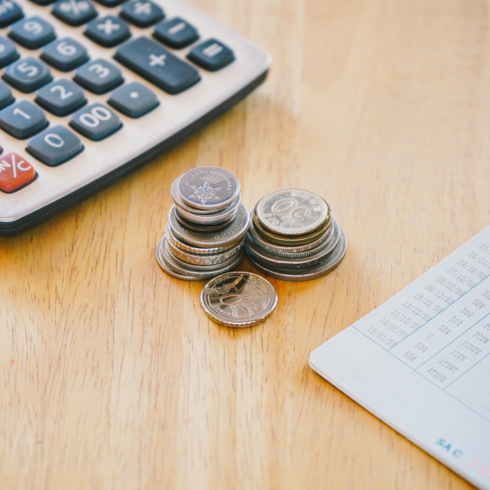 Stack of money coin on woo office desk with bank book and calculator.